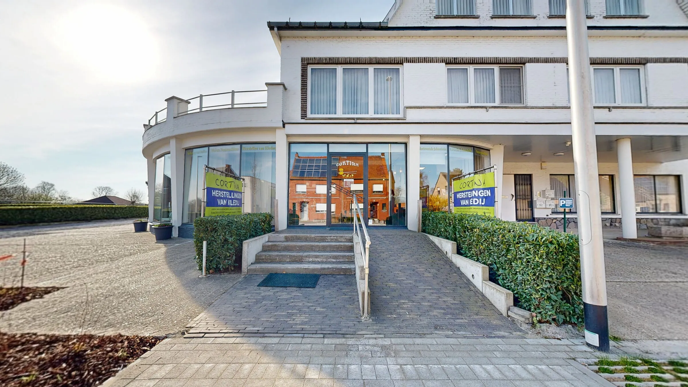 De voorgevel van Cortina met vlaggen “Herstellingen van kledij” en een helling naar de ingang